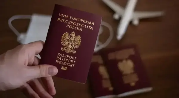 Dłoń trzyma polski paszport. Obok leżą kolejne dokumenty, maseczka i model samolotu. Planujesz podróż i zastanawiasz się, jak wyrobić paszport?