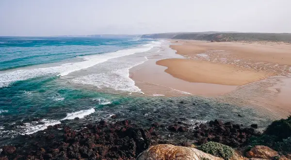 Piękne plaże i turkusowe morze, idealne na algarve wakacje. Surferzy łapią fale, a skały tworzą malowniczy brzeg.