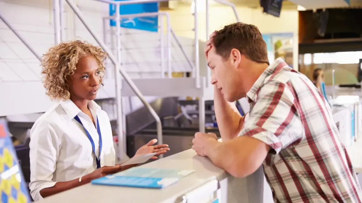 Zestresowany mężczyzna przy stanowisku check-in, rozmawia z pracownicą lotniska.