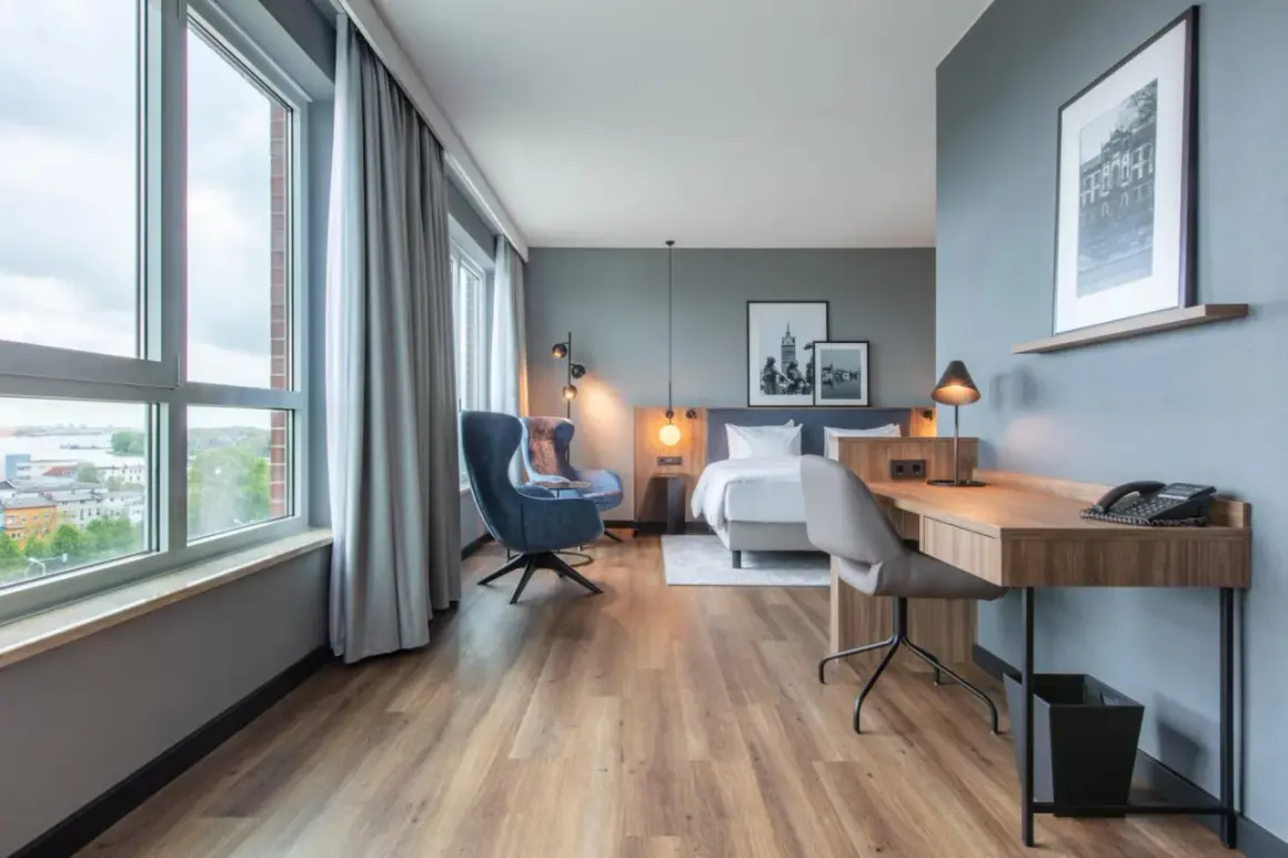 Nowoczesny pokój w **Radisson Blu Hotel Rostock** z widokiem na miasto, łóżkiem, fotelem i biurkiem.