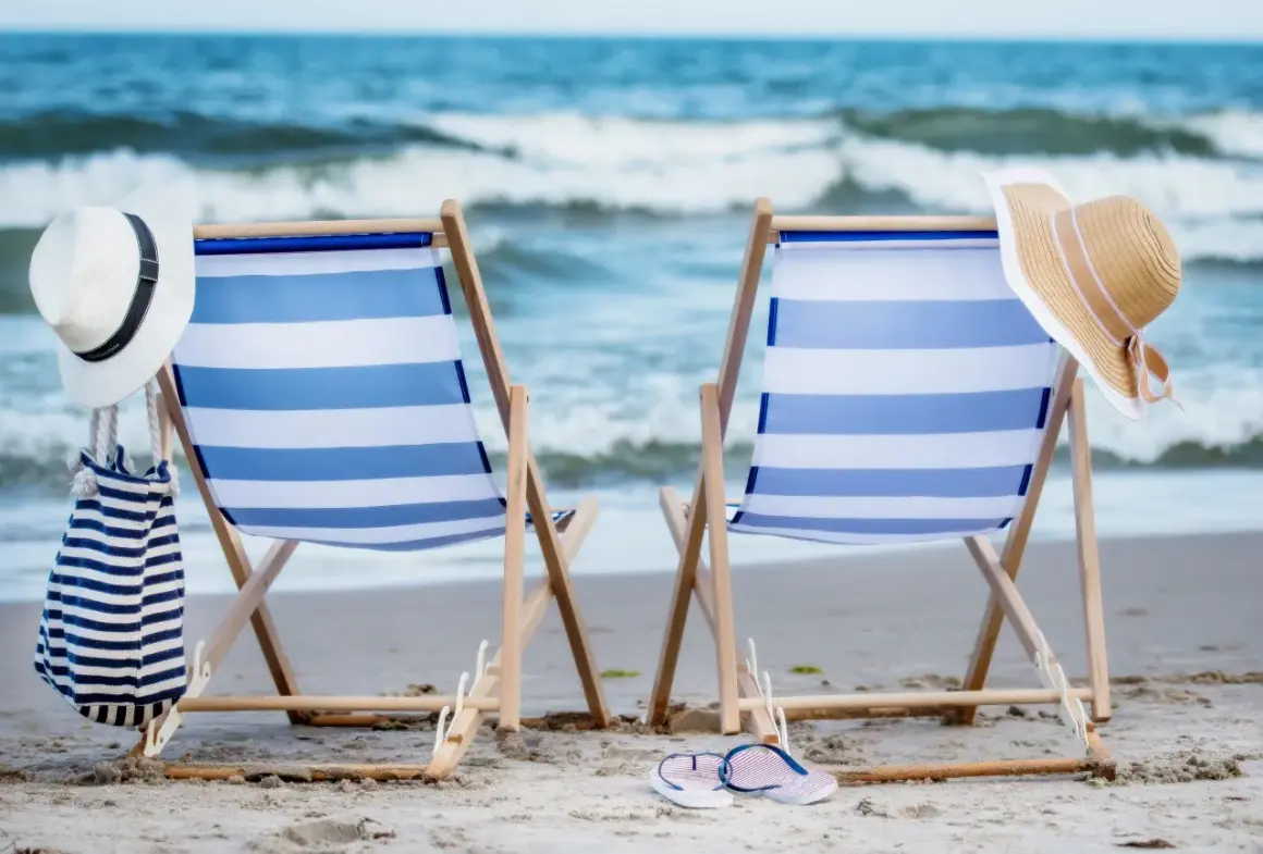 Dwa leżaki na plaży, gotowe na idealny weekend nad morzem. W tle widać morze i fale.