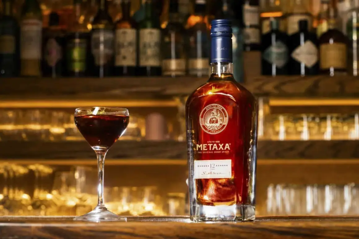 Butelka greckiego alkoholu Metaxa 12 gwiazdek i kieliszek z ciemnym trunkiem na tle baru.