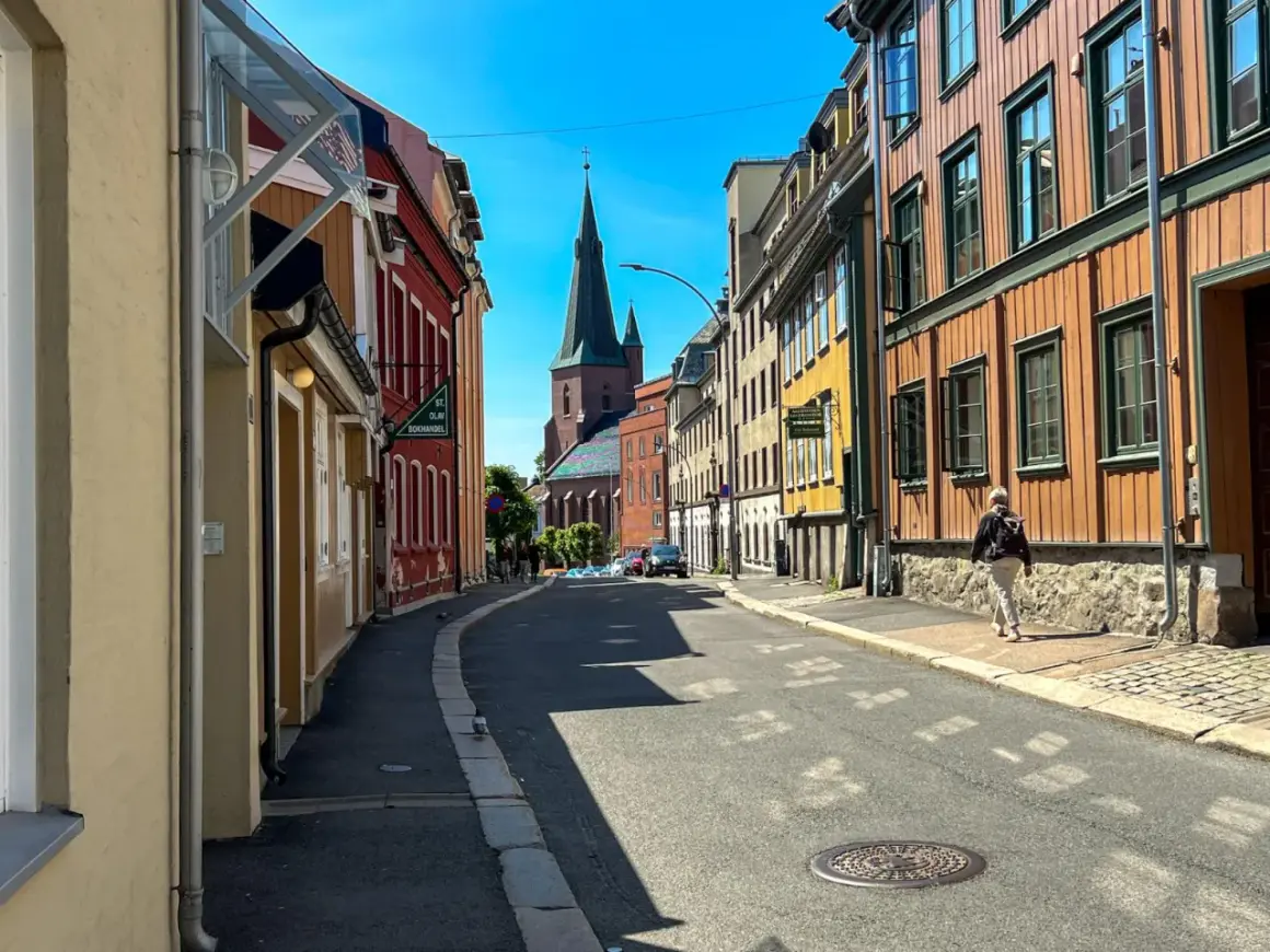 Ulica w Oslo z kolorowymi kamienicami i kościołem w tle.