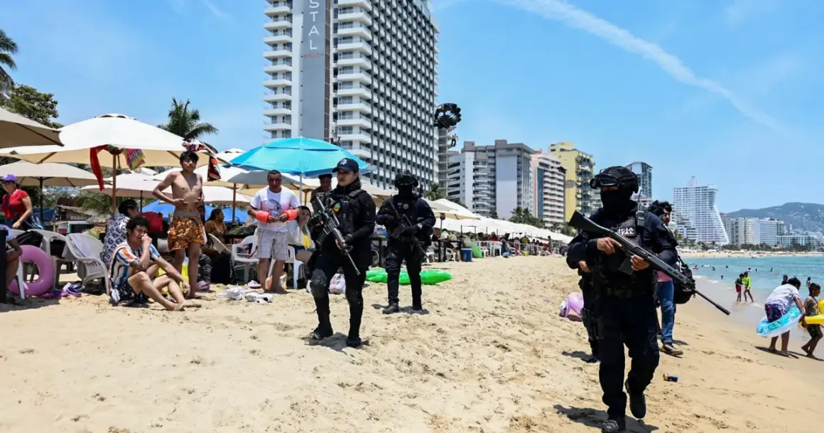 Meksyk zamieszki na plaży. Policjanci w pełnym rynsztunku patrolują brzeg, podczas gdy turyści odpoczywają pod parasolami.