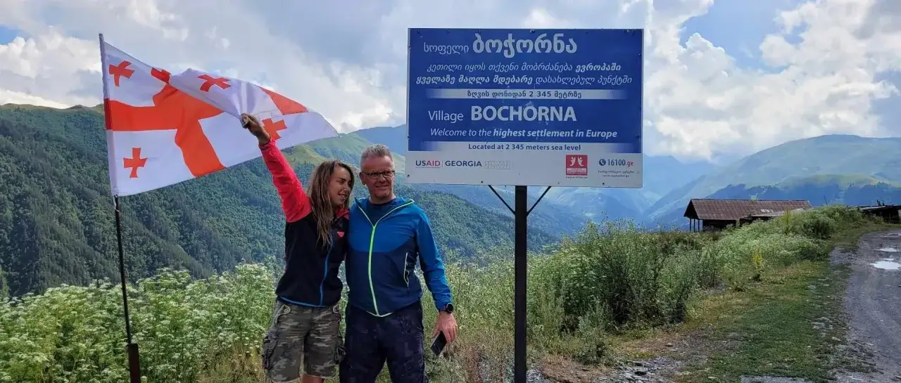 Para, z gruzińską flagą, na tle gór i tablicy