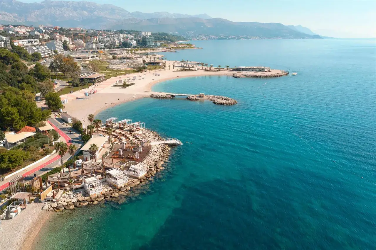 Widok na plażę i morze z hotelu Radisson Blu Split. Woda jest turkusowa, a plaża piaszczysta z leżakami i parasolami.