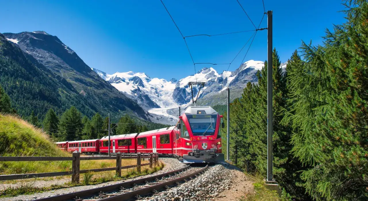 Czerwony pociąg Bernina Express wjeżdża na malowniczą trasę, mijając alpejskie szczyty i zielone lasy. Idealna wycieczka dla miłośników górskich krajobrazów.