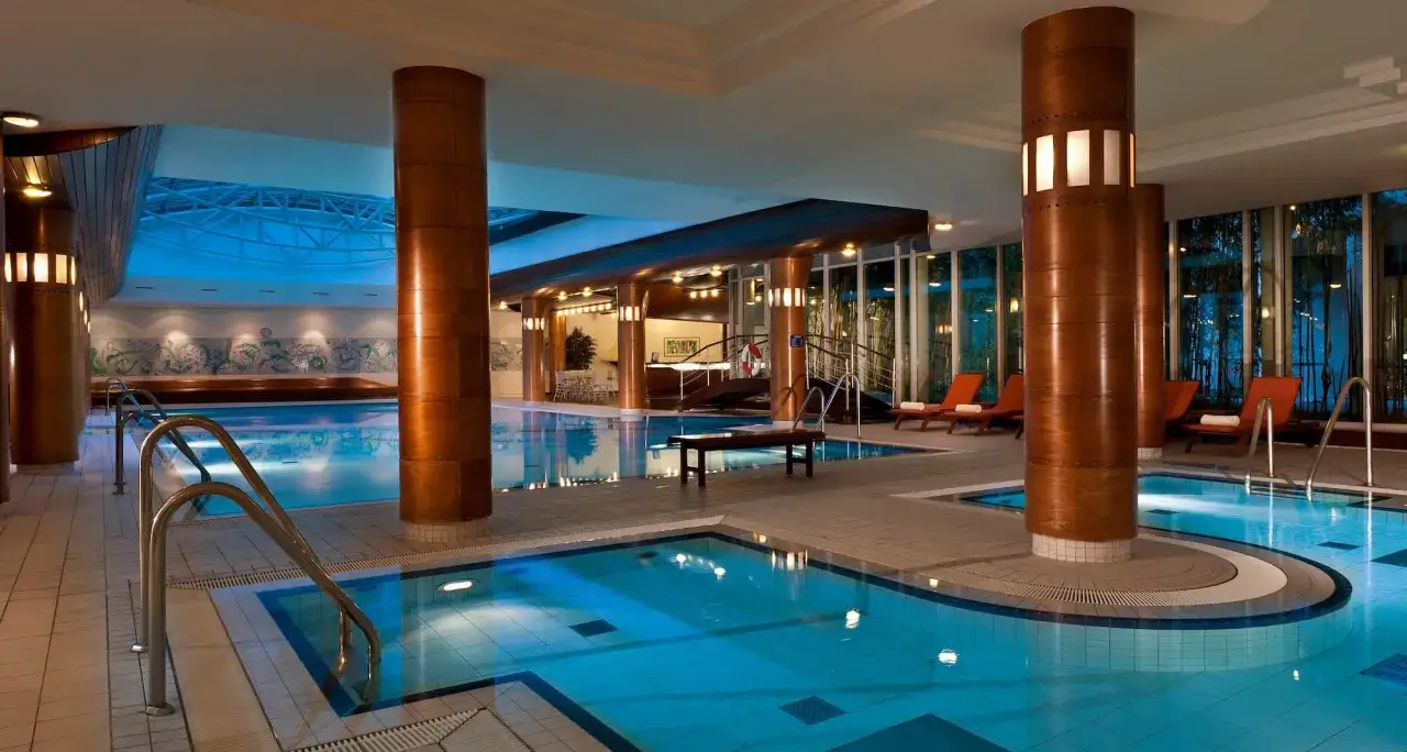 Basen w hotelu Radisson Blu Radebeul, z niebieską wodą, drewnianymi kolumnami i leżakami.