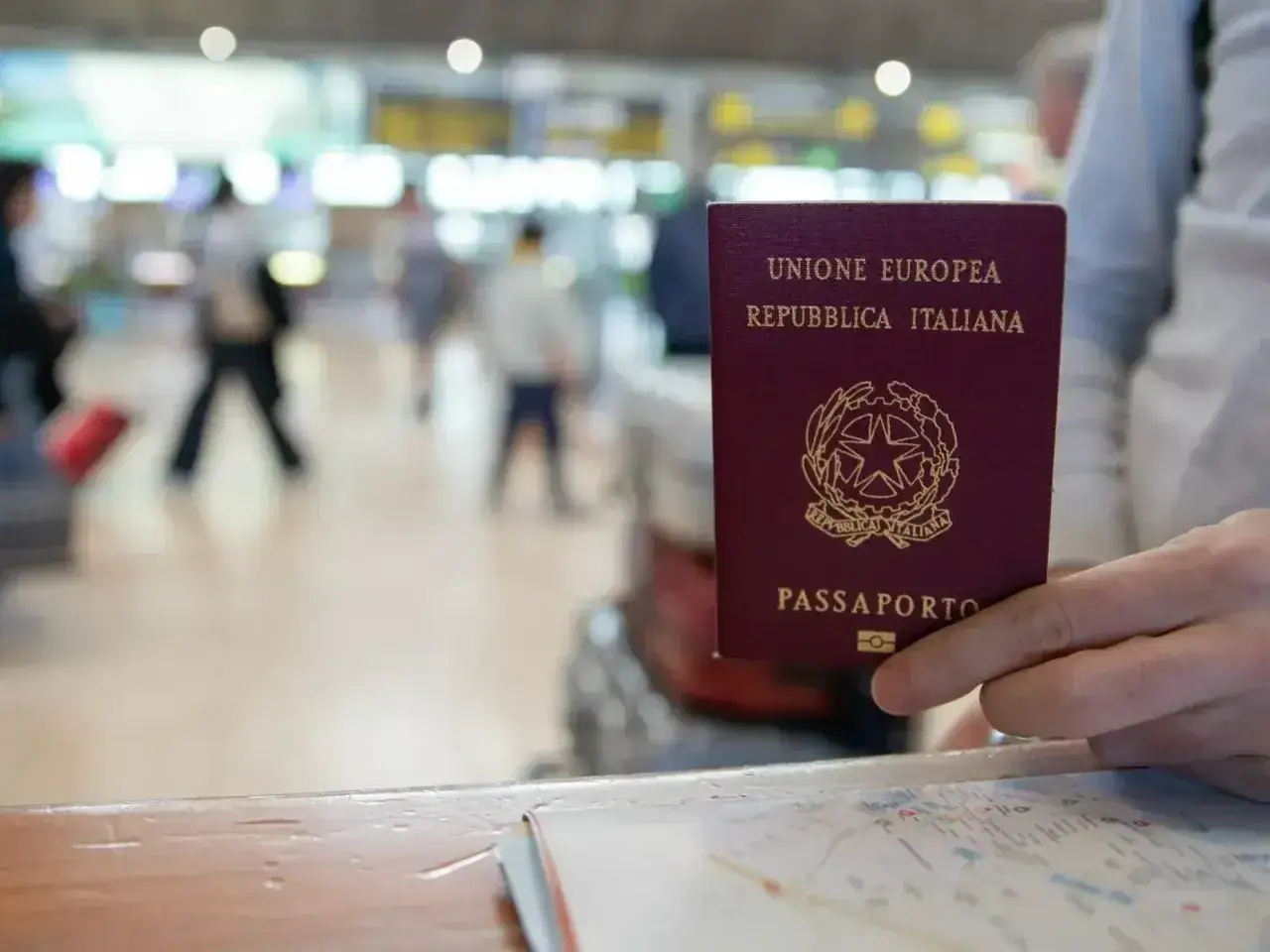 Włoski paszport w dłoni, w tle lotnisko. Czy do Serbii potrzebny jest paszport? Zależy od obywatelstwa.