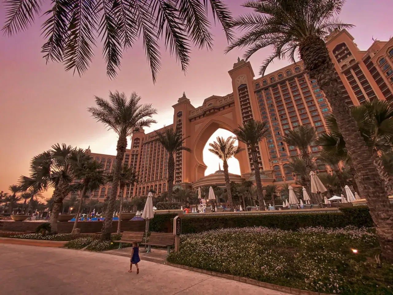 Zachód słońca nad hotelem Atlantis w Dubaju, z palmami i łukiem w architekturze.