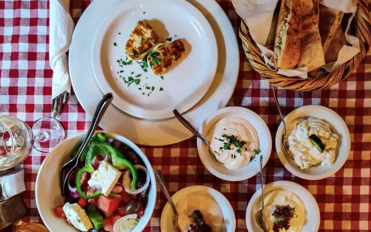 Pyszne jedzenie z Cypru: sałatka grecka, halloumi, dipy i pieczywo na czerwonym obrusie.