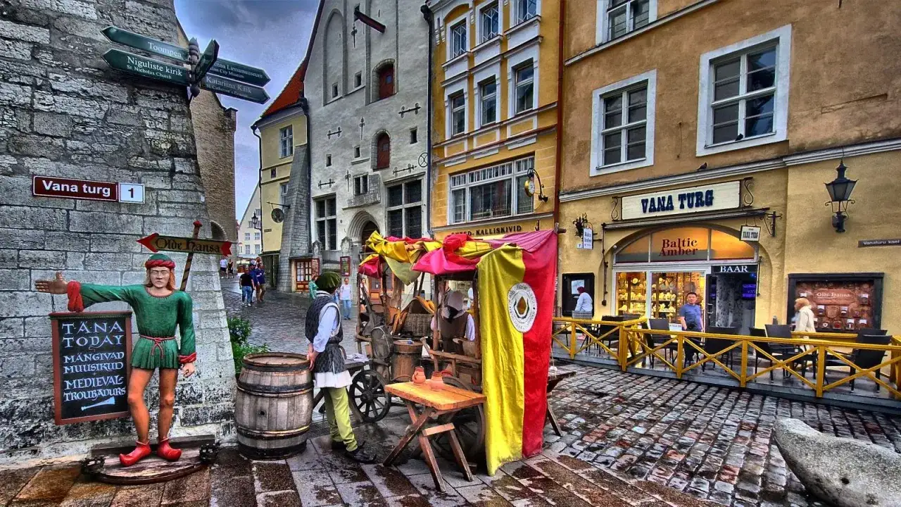 Ulica w stolicy Estonii, Tallinnie, z historycznymi budynkami, straganem i postacią trubadura.