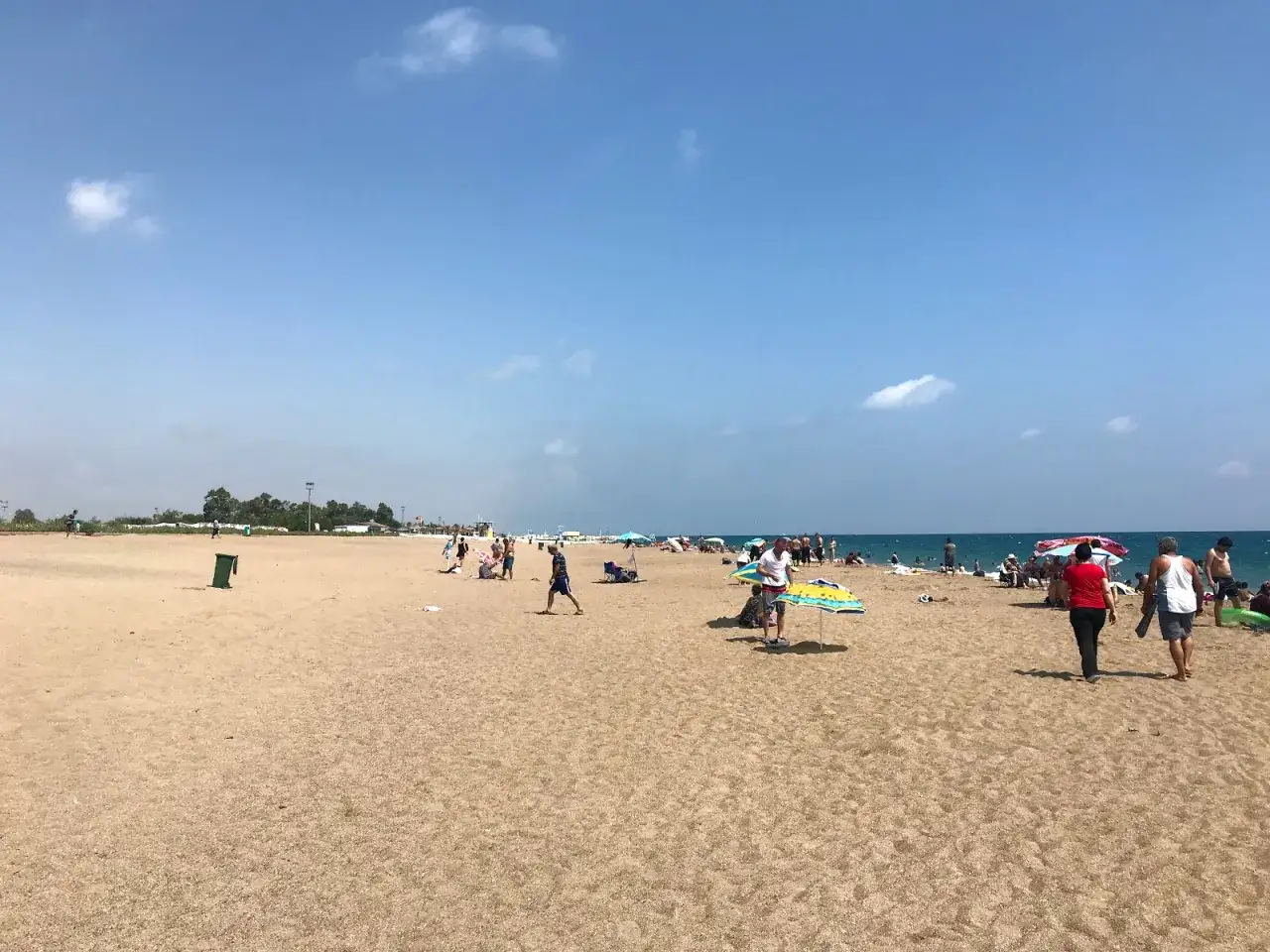 Słoneczny dzień na plaży w Lara, Turcja. Ludzie odpoczywają pod parasolami, spacerują po piasku i kąpią się w morzu.