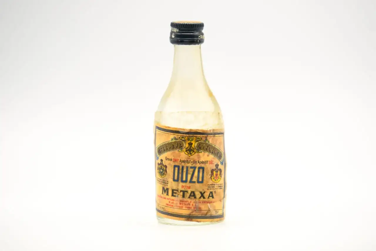 Mała butelka greckiego alkoholu Ouzo Metaxa, z etykietą w kolorze złota i niebieskim napisem.
