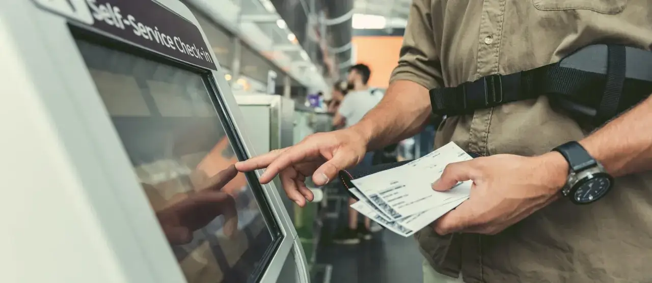 Mężczyzna z biletami w ręku dokonuje check-in przy automacie samoobsługowym.