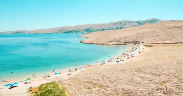Turkusowe jakie morze jest w Chorwacji? Piękna plaża z ludźmi, parasolami i górami w tle.
