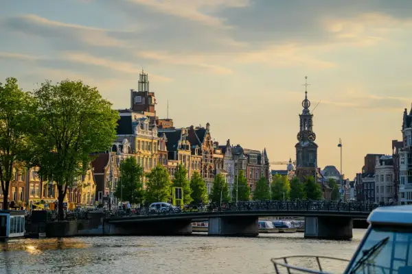 Złota godzina nad kanałem, gdzie jest Amsterdam. Wąskie kamienice, most pełen rowerów i łodzie na wodzie.