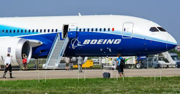 Ogromny samolot Dreamliner Boeing z otwartymi drzwiami i schodkami. W tle ludzie i sprzęt lotniskowy.