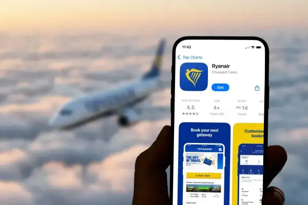 Telefon z aplikacją Ryanair, gotowy do odprawy online. W tle samolot lecący nad chmurami.