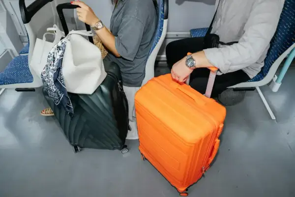 Podróżni z bagażem podręcznym: czarna walizka i jaskrawo pomarańczowa walizka stoją obok siebie w pociągu.