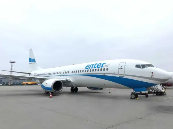 Biały samolot Enter Air z niebieskimi pasami na tle pochmurnego nieba. Gotowy do startu, by zabrać pasażerów w podróż.
