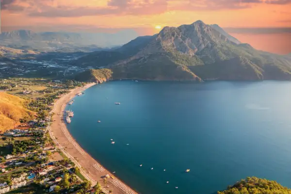 Widok z lotu ptaka na wybrzeże Turcji. Piękne turkusowe morze, piaszczysta plaża z leżakami i góry w tle o zachodzie słońca.