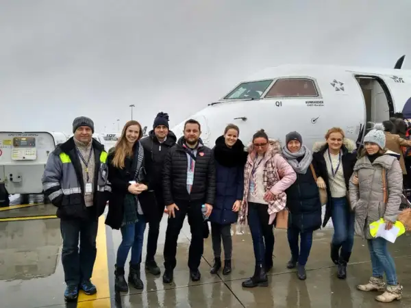 Grupa osób pozuje przed samolotem Bombardier Q400, z logo IATA na kadłubie.