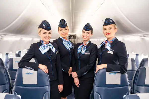 Uśmiechnięte stewardessy linii Enter Air w granatowych mundurkach i chustach z logo firmy, gotowe do lotu.