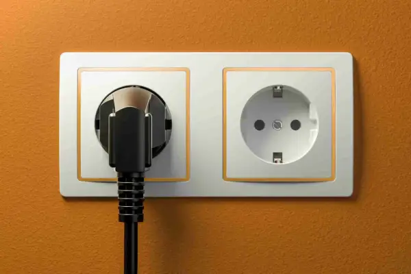Dwa gniazdka elektryczne, jedno z wtyczką, na pomarańczowej ścianie. Typowe gniazdka w Turcji.
