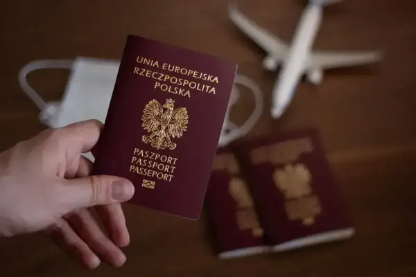 Dłoń trzyma polski paszport. Obok leżą inne paszporty, maseczka i samolot. Zastanawiasz się, ile trwa wyrobienie paszportu?
