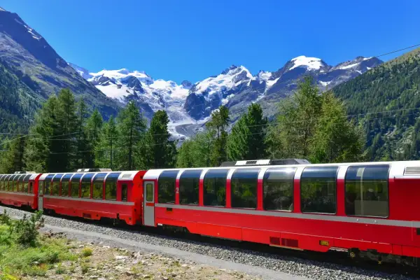 Czerwony pociąg Bernina Express w malowniczej scenerii Alp. Wycieczka przez góry z widokiem na ośnieżone szczyty i zielone lasy.