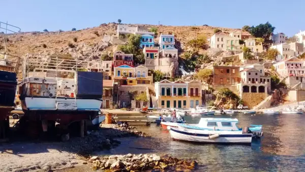 Kolorowe domy na zboczu góry, łodzie w zatoce i kamienista plaża na wyspie Symi.