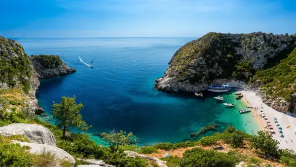 Malownicza zatoka z krystalicznie czystą wodą i plażą, gdzie cumują łodzie. Idealne miejsce na wakacje, zastanawiasz się, ile się leci do Albanii?